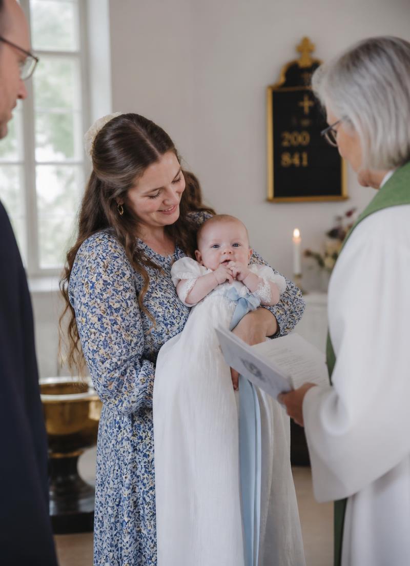 Dåp i kirke, baby i dåpskjole holdt av forelder