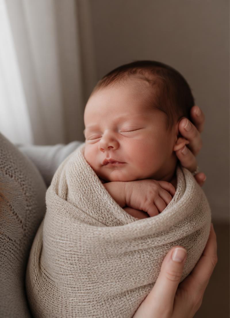 Sovende nyfødt baby svøpt i strikket teppe i mors hender